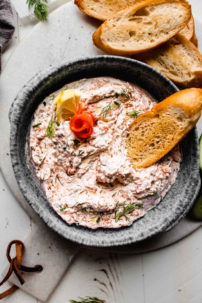 Bowl of smoked salmon dip with piece of crostini dipped into it.