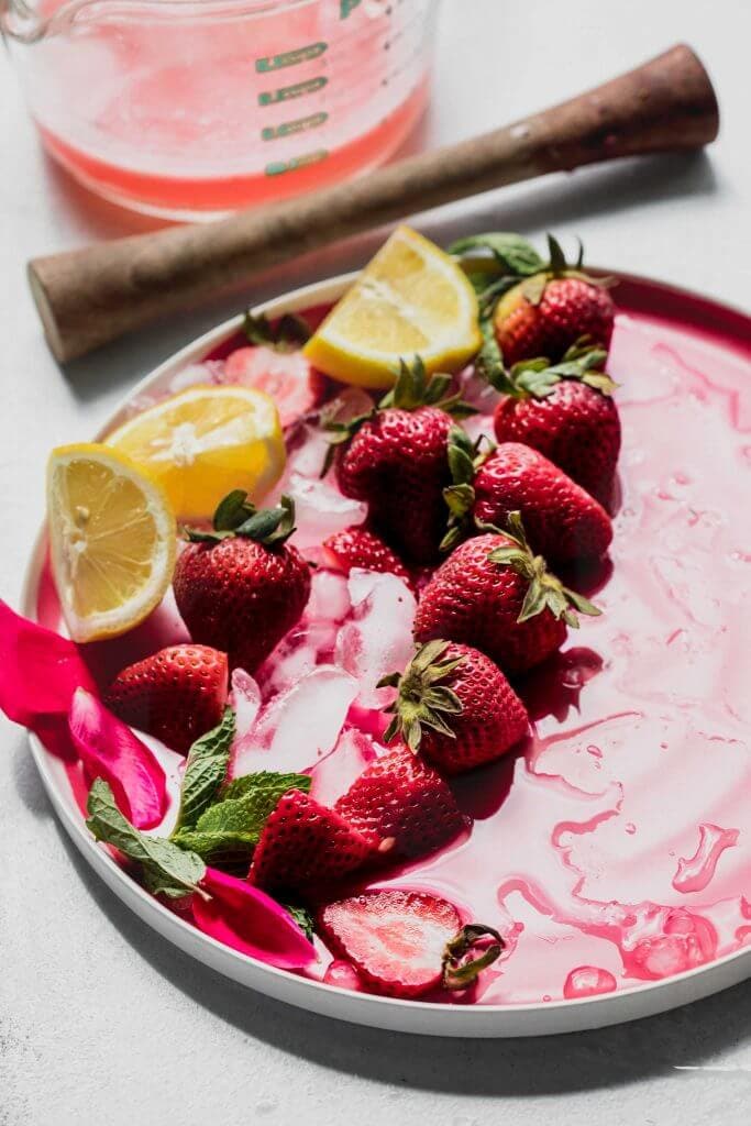 Strawberries and lemons scattered on pink plate.