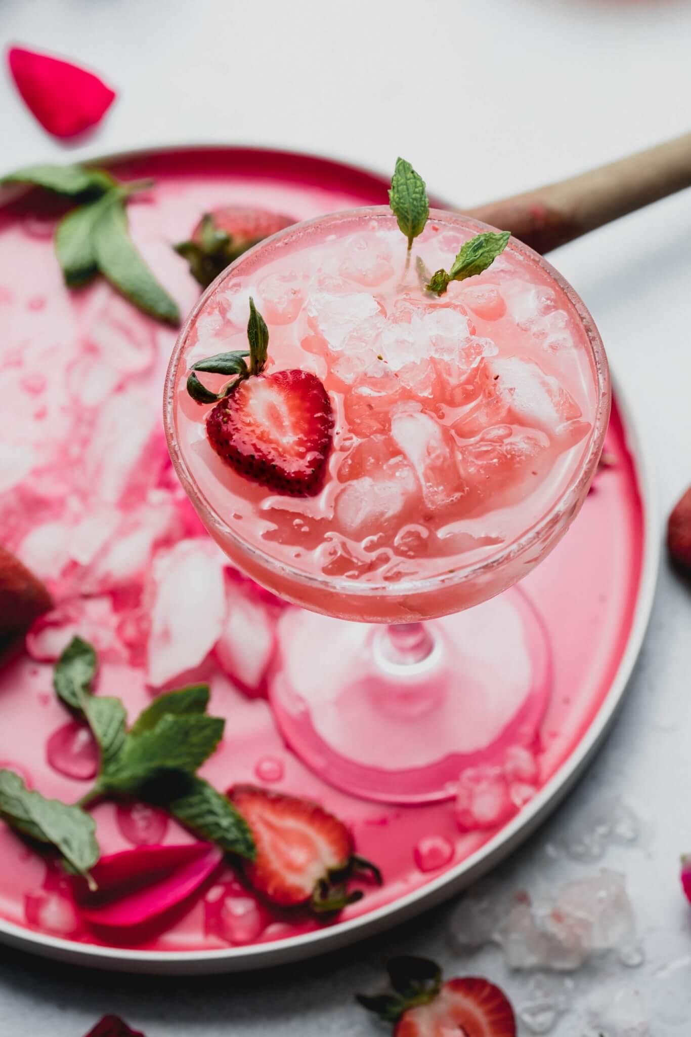 Strawberry white wine spritzer displayed on pink plate with strawberries scattered about.