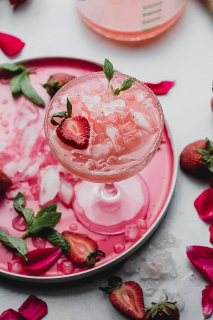 Strawberry white wine spritzer displayed on pink plate with strawberries scattered about.