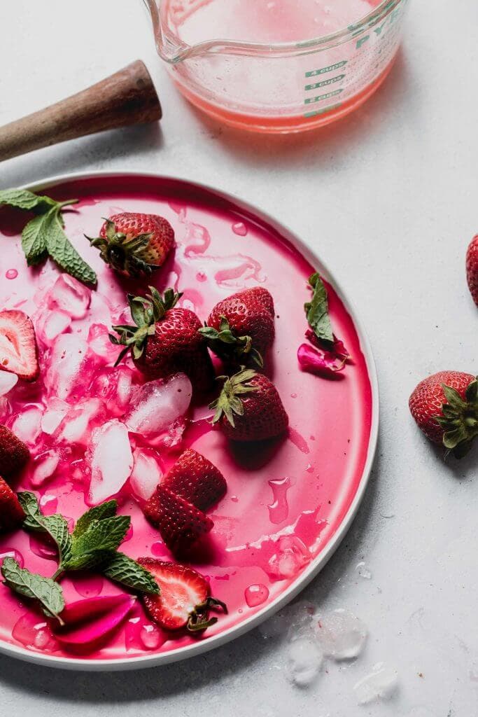 Strawberries and lemons scattered on pink plate.