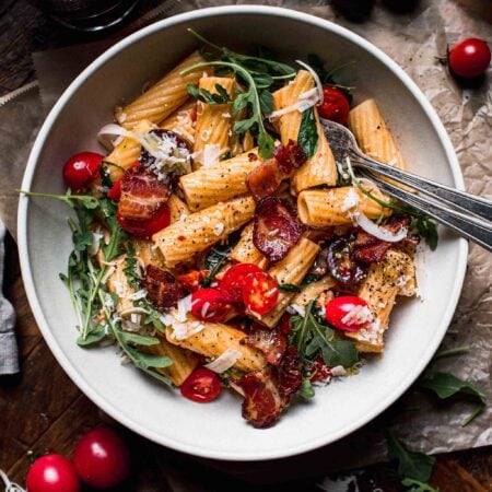 Overhead shot of blt pasta in white bowl on wood background next to glass of wine.