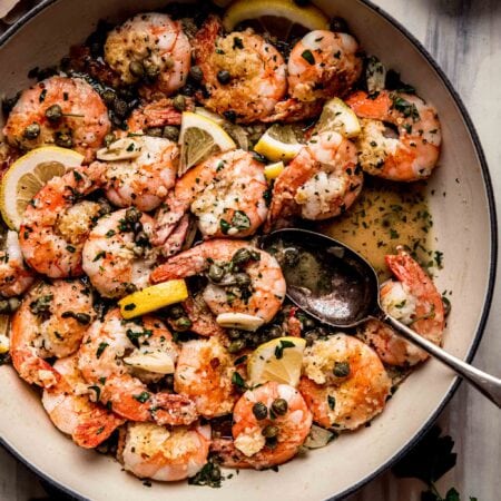 Skillet filled with shrimp piccata on pink backdrop.