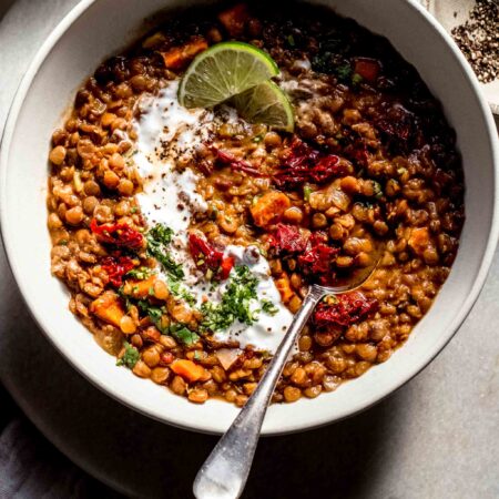 Overhead shot of bowl of lentil soup topped with chopped chipotles and served with spoon.