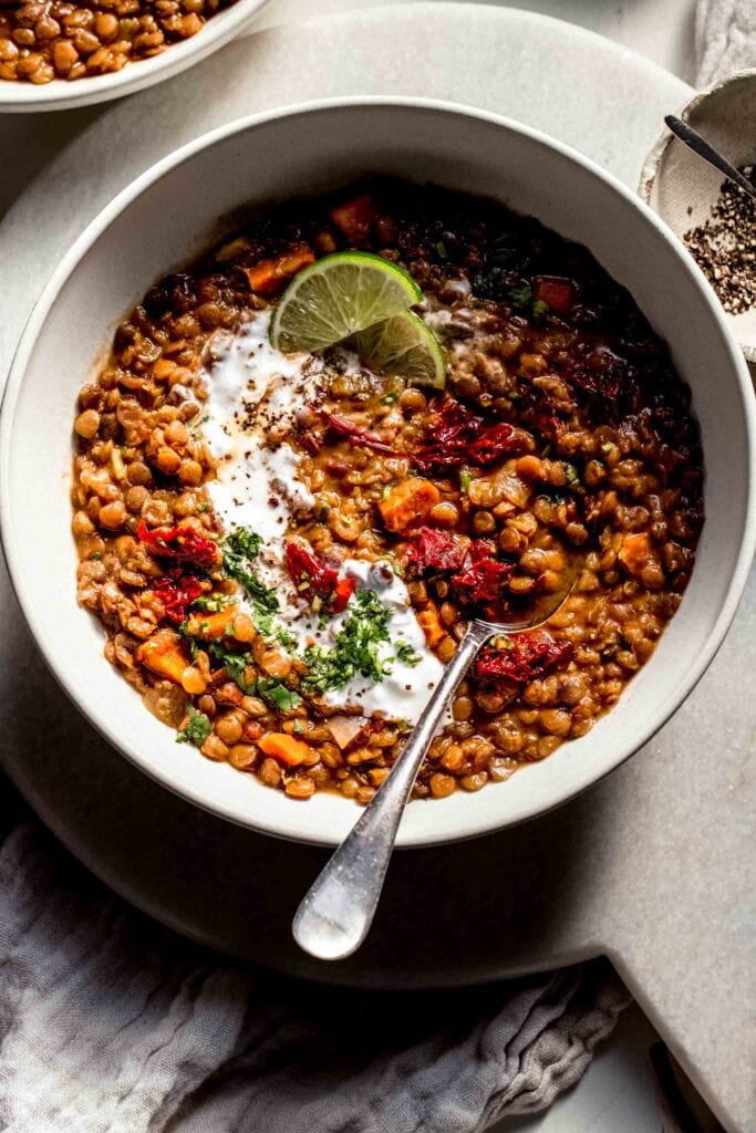 Overhead shot of bowl of lentil soup topped with chopped chipotles and served with spoon. 