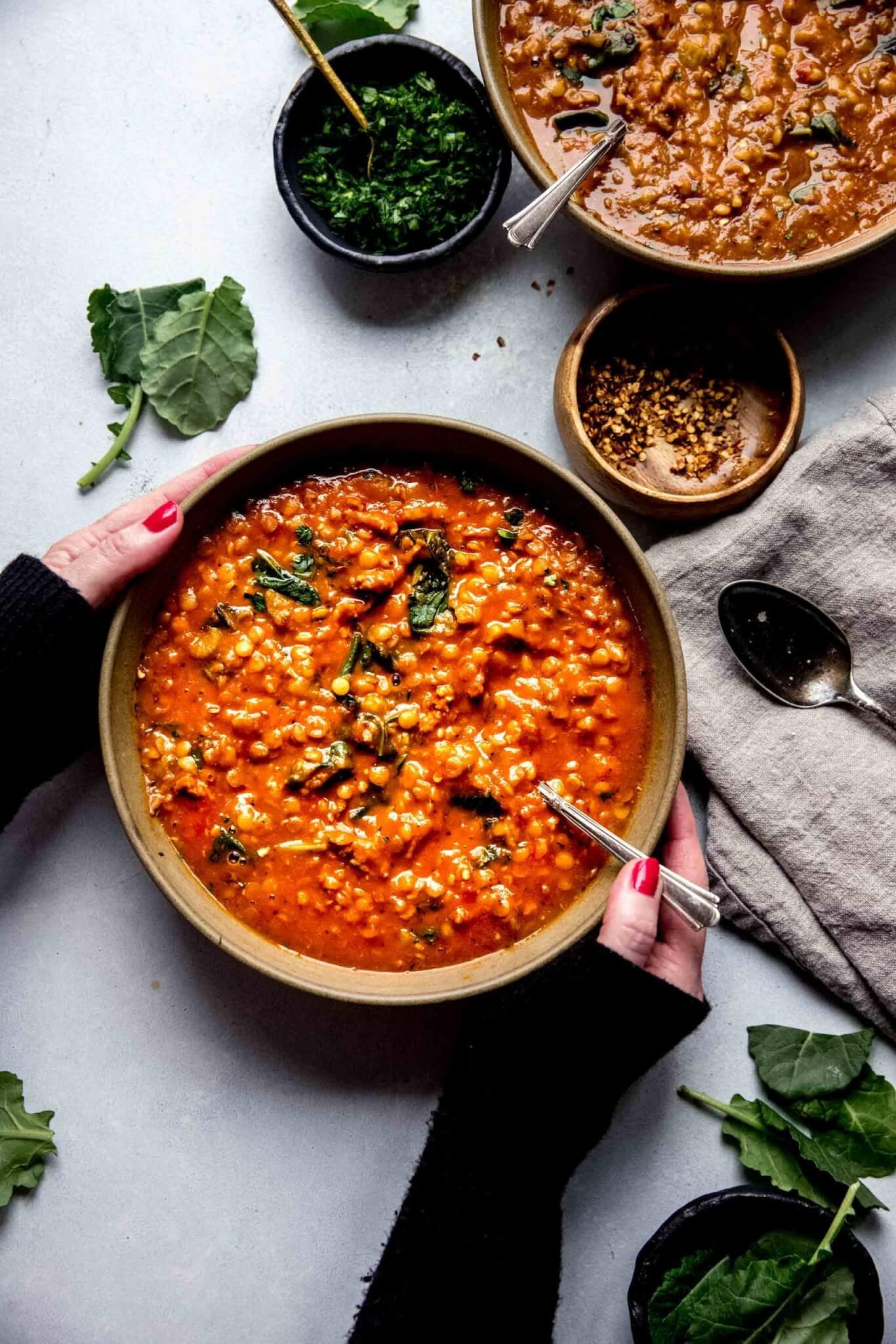 Hands holding bowl of lentil soup with sausage.