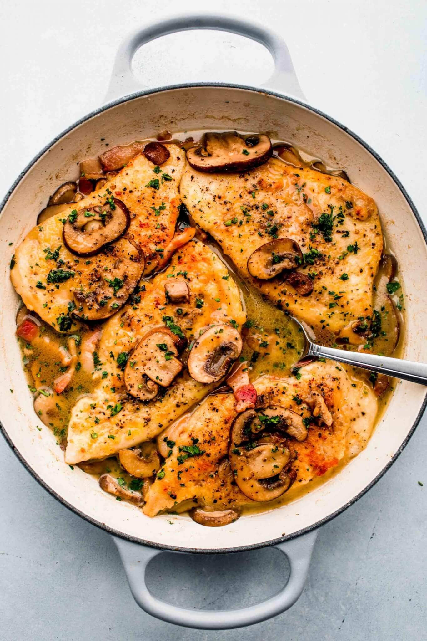 Chicken marsala in large skillet with spoon in sauce.