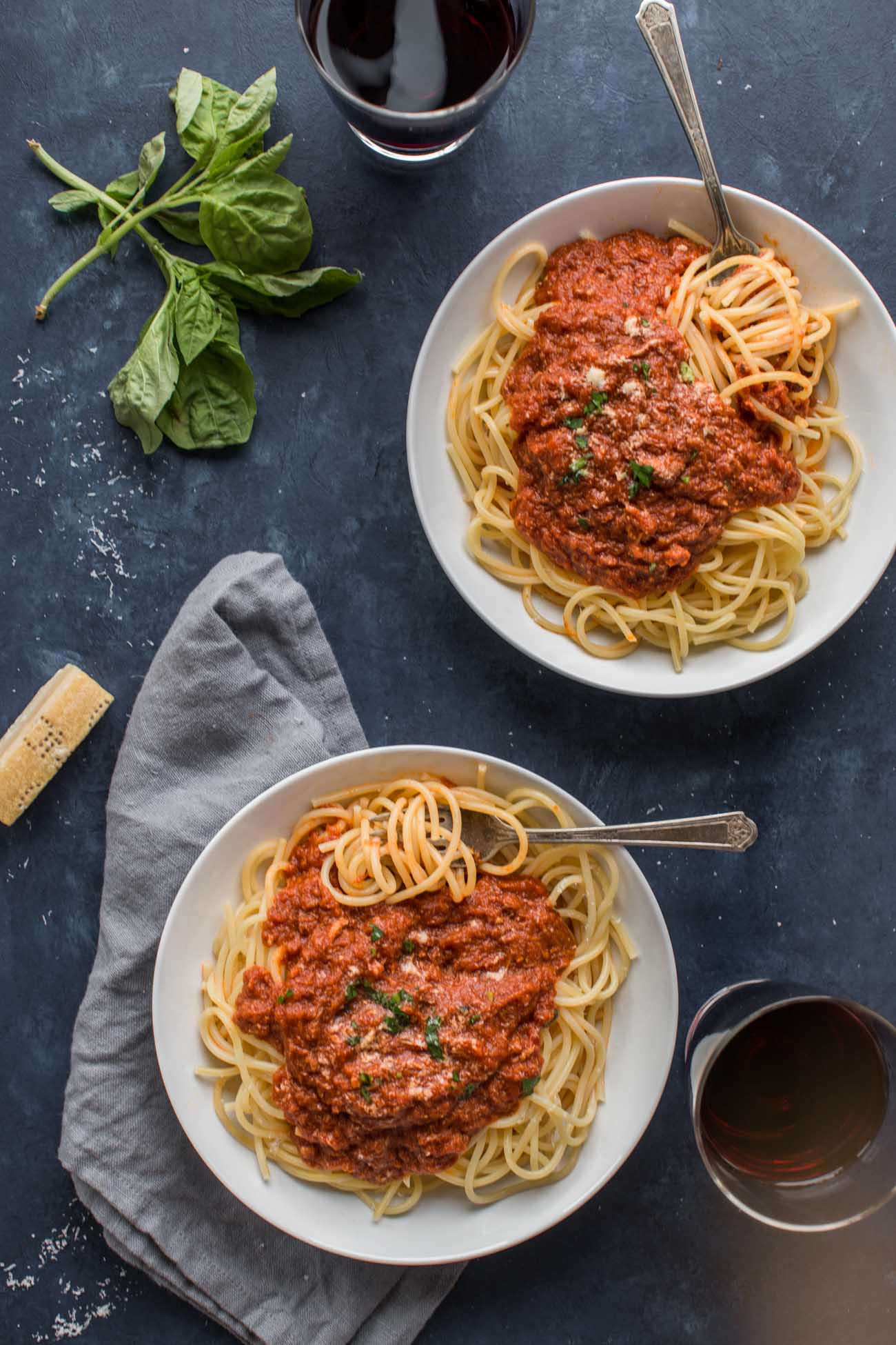 Two bowls of Sunday Gravy ready to eat with forks and parmesan cheese, next to glasses of wine. 