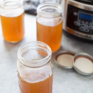Jars of slow cooker bone broth with crockpot in background.