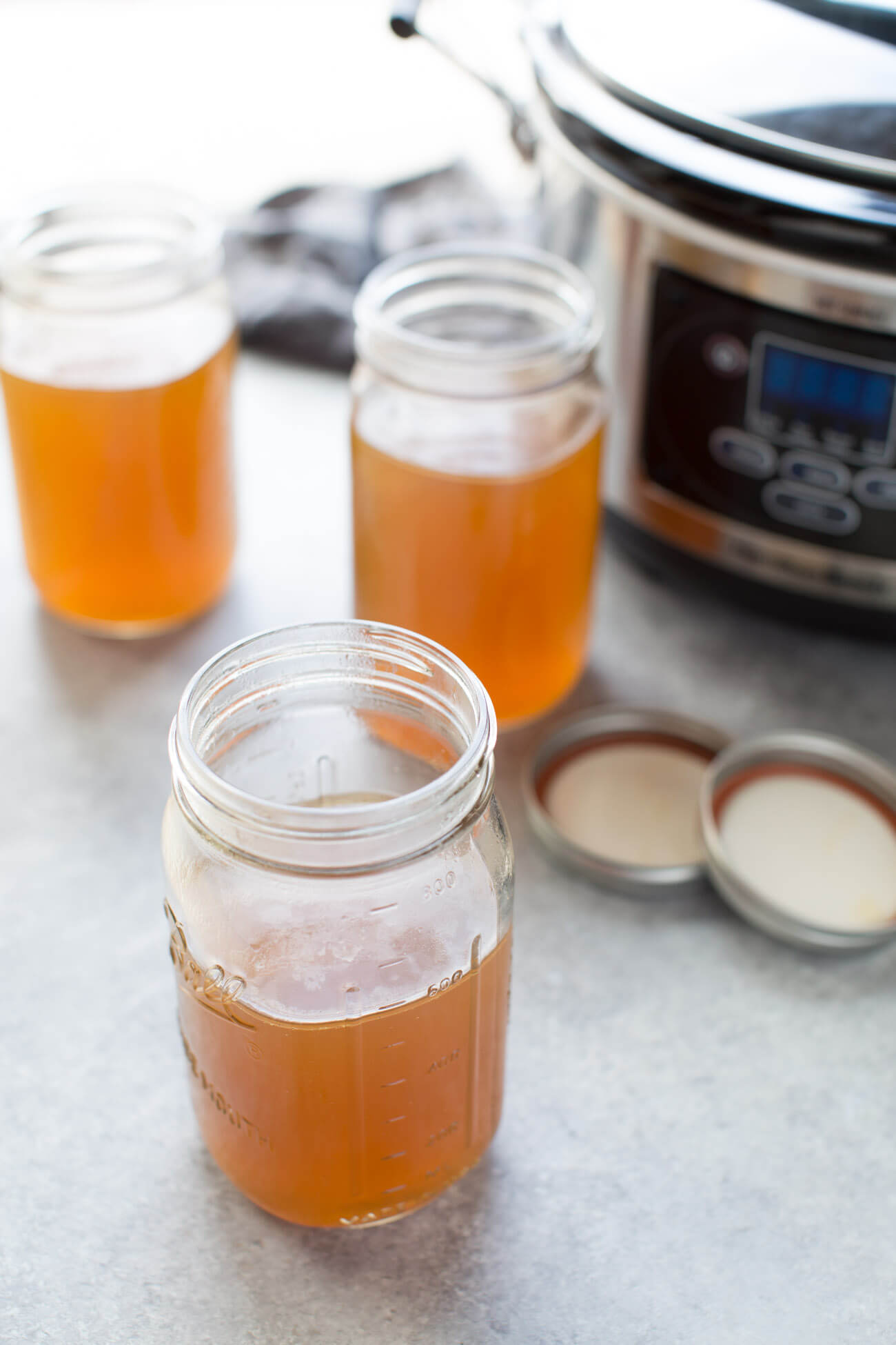 Jars of slow cooker bone broth with crockpot in background.