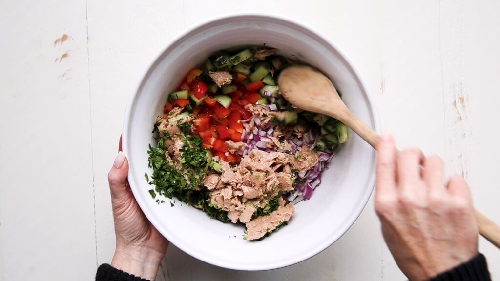Tuna chickpea salad ingredients being mixed together in bowl. 