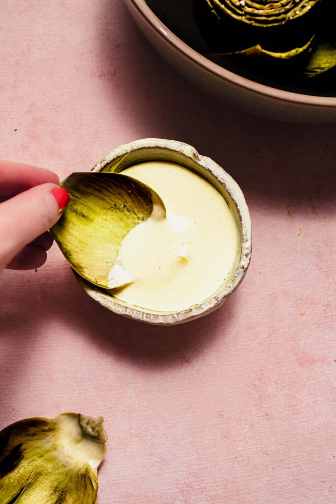 Hand dipping artichoke leaf into sauce. 