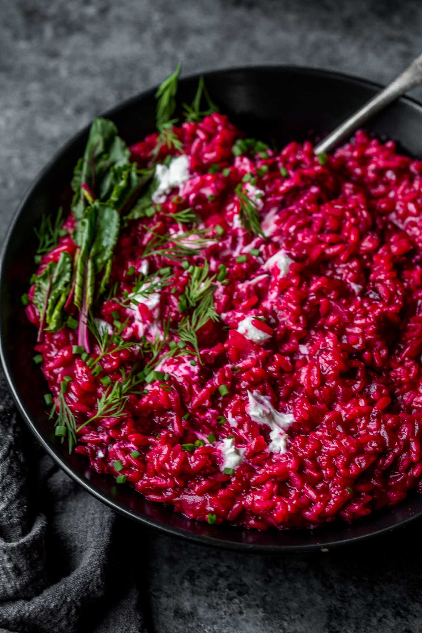 Beet risotto in black bowl.