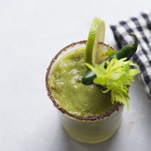 Green bloody mary in glass garnished with lime wheel and celery stalk.