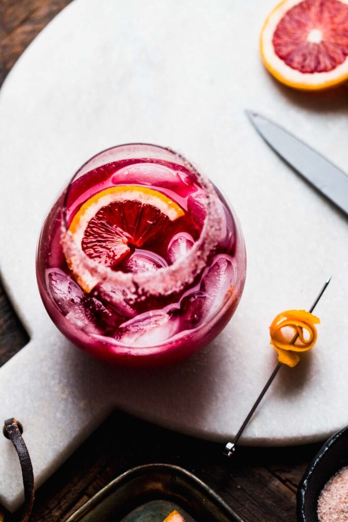 Hibiscus margarita in salt rimmed glass garnished with grapefruit wedge on white serving tray.