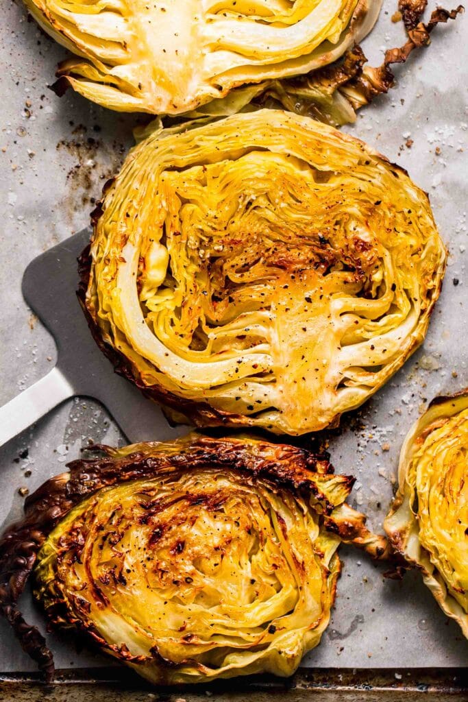 Roasted cabbage steaks on baking sheet with spatula.