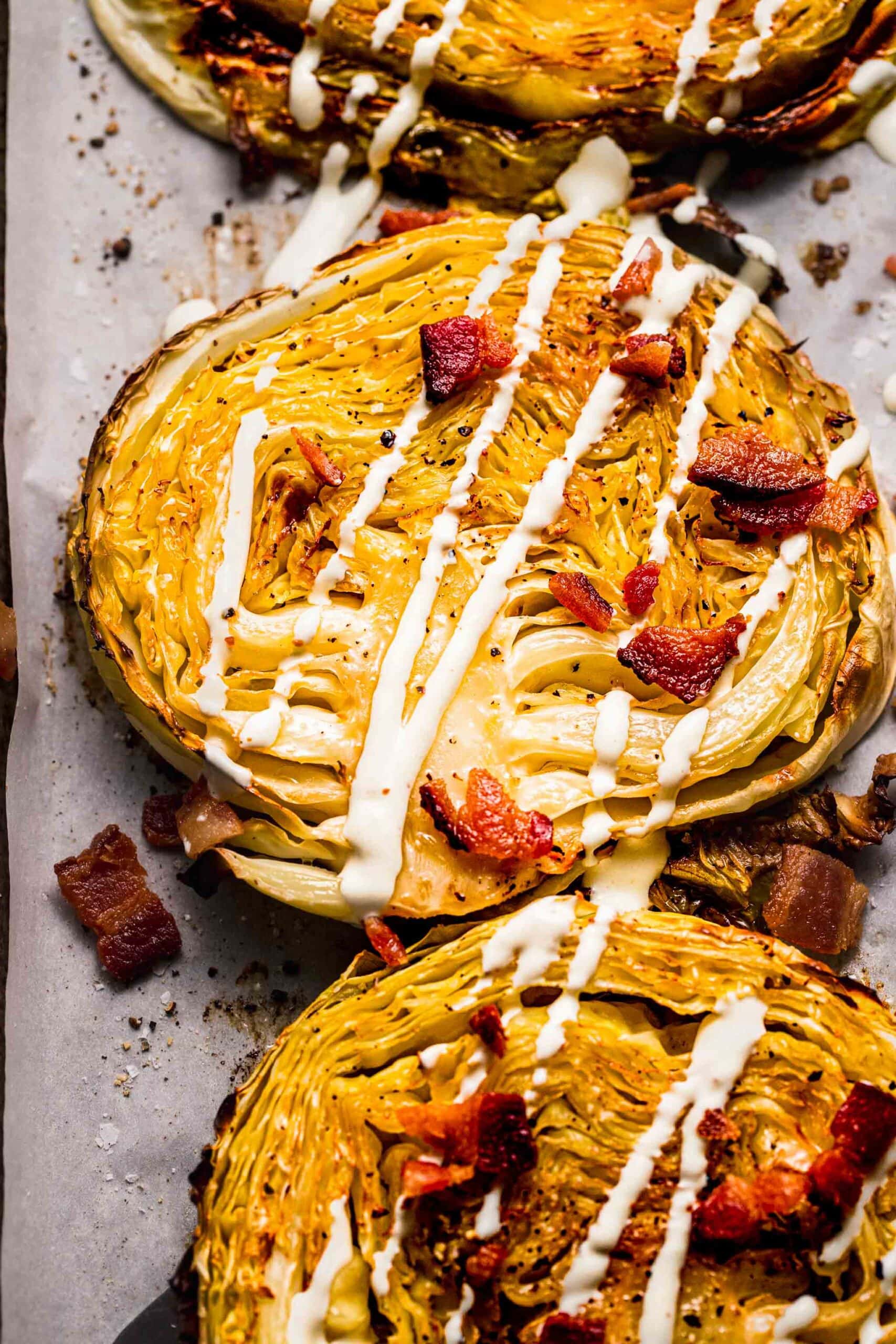 Close up of roasted cabbage steaks topped with bacon and drizzled with cream sauce.