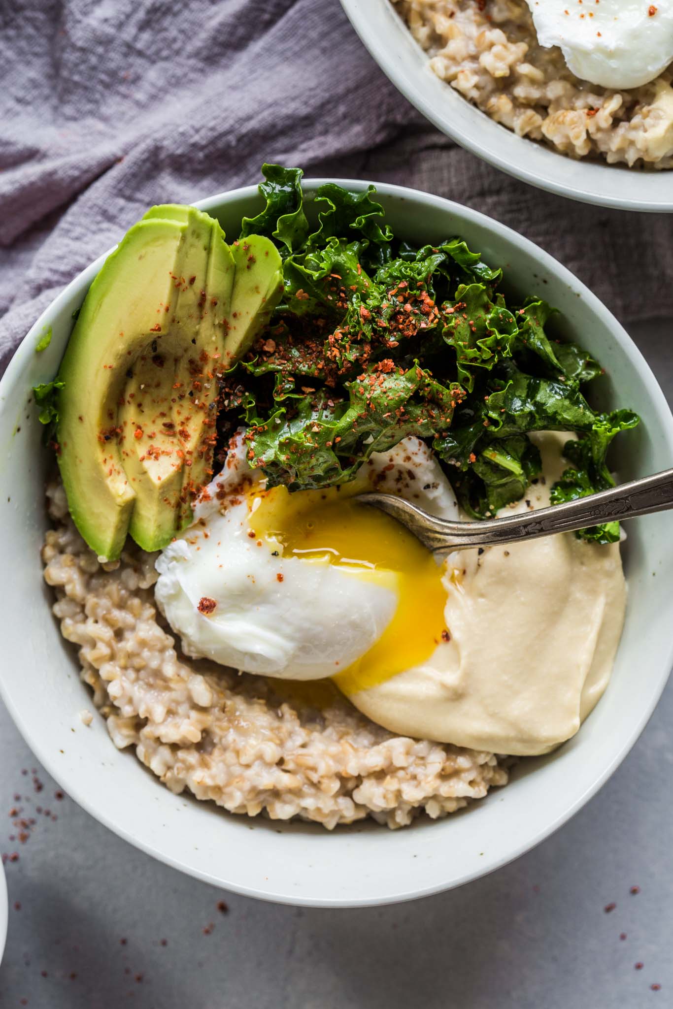 Avocado & Kale Savory Oat Bowls are the perfect way to start your day. Hearty oatmeal is topped with avocado, lemony kale salad, hummus and aleppo pepper for a protein-packed breakfast.