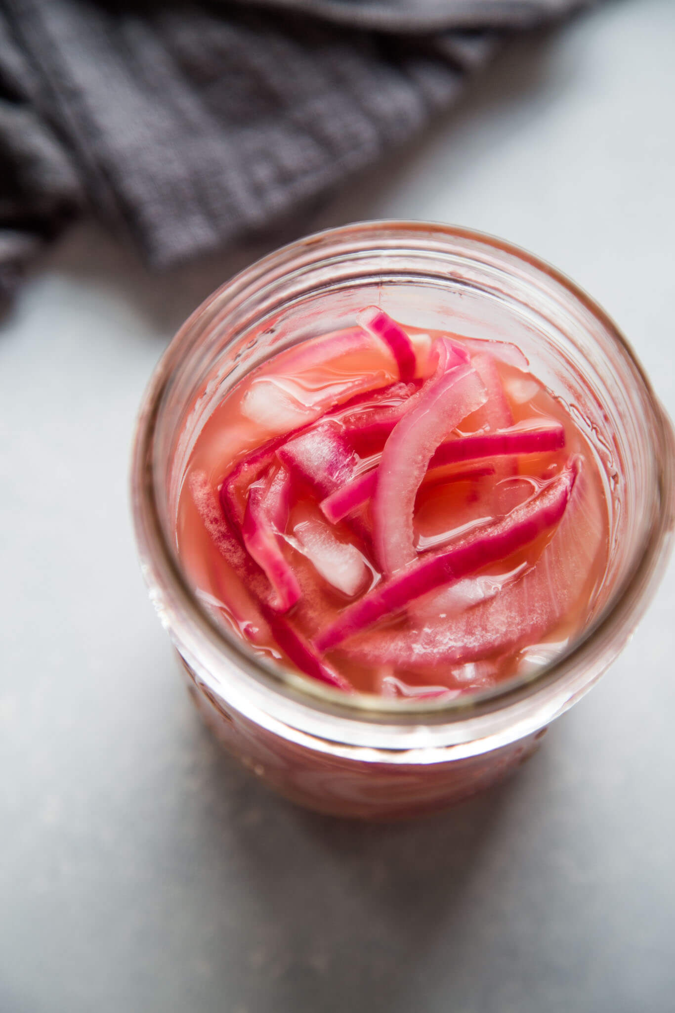 Overhead shot of jar of pickled onions next to dark grey dish cloth.