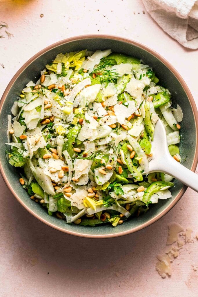 Overhead shot of shaved fennel salad in green serving bowl on pink table.