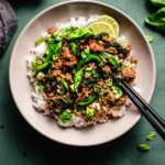 Thai Beef Stir Fry in bowl with chopsticks on dark green background.