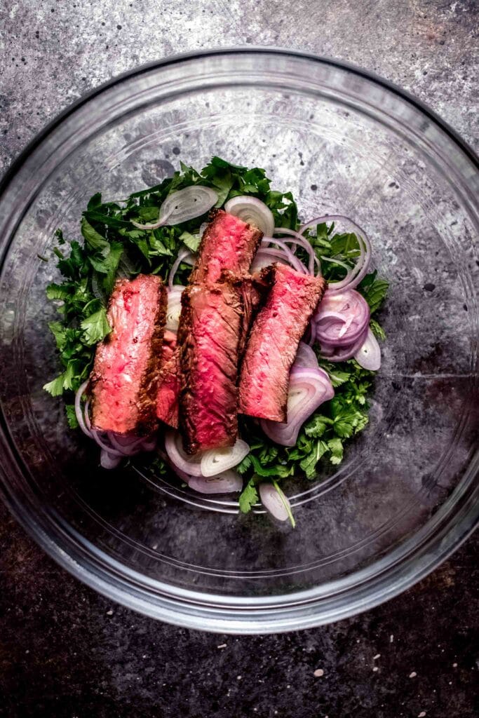 Sliced steak in bowl with fresh herbs. 