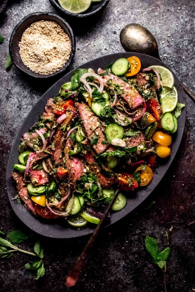 Thai steak salad next to bowl of rice powder. 