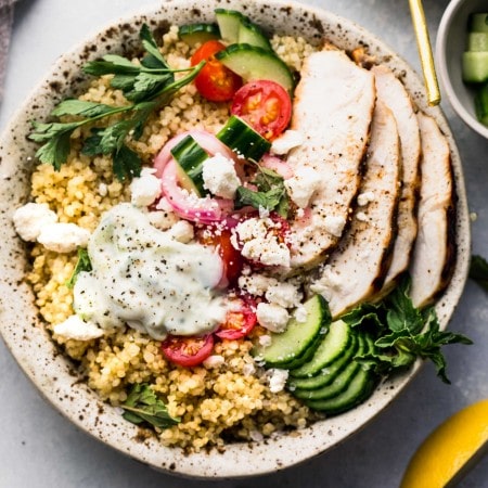 Overhead shot of quinoa gyro bowl topped with cucumbers, tomatoes, next to bowl of tzatziki sauce.