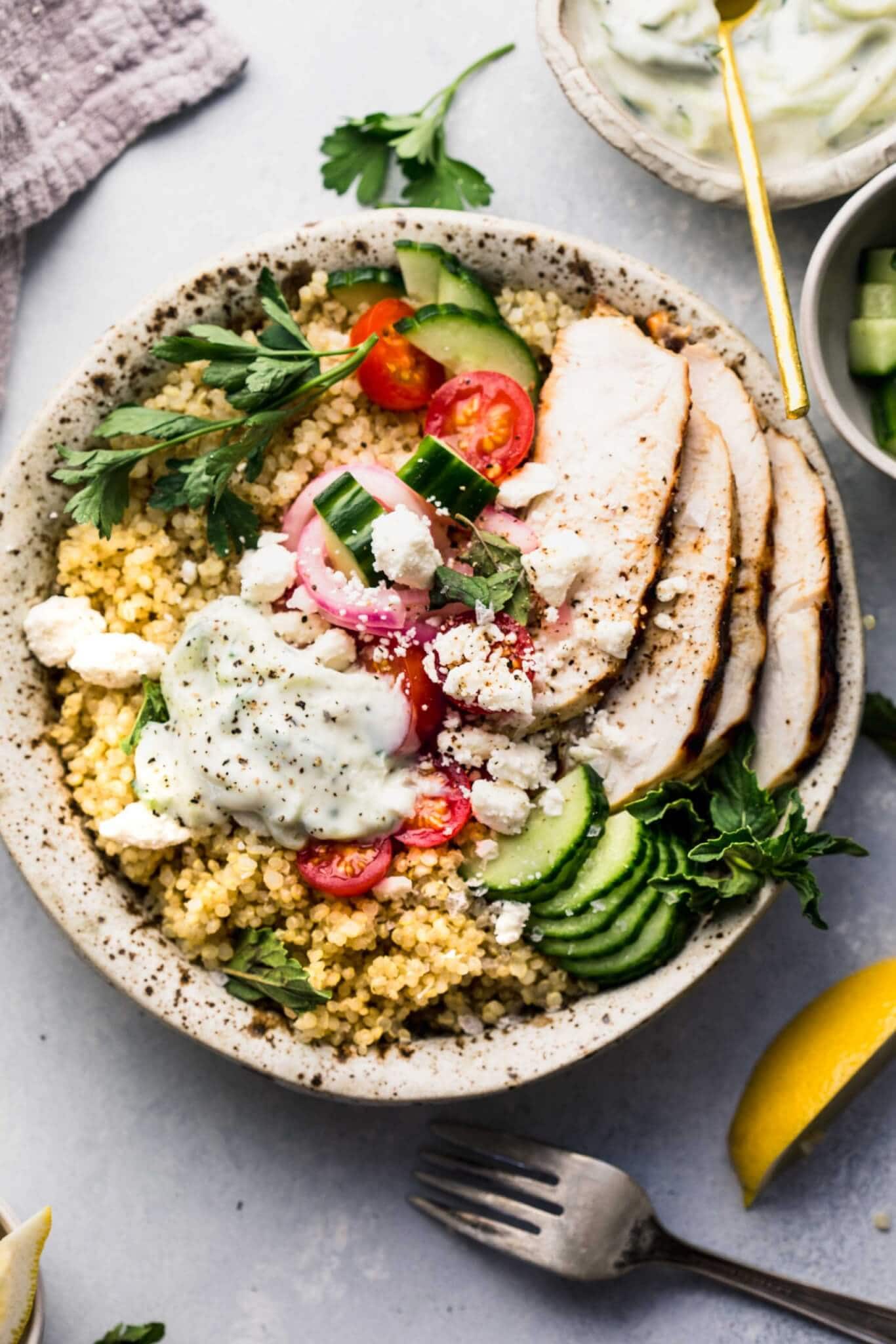 Overhead shot of quinoa gyro bowl topped with cucumbers, tomatoes, next to bowl of tzatziki sauce.