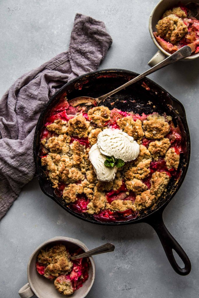 Strawberry rhubarb cobbler in cast iron skillet topped with scoops of ice cream. 