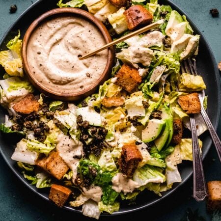 Overhead shot of vegan caesar salad on plate with small bowl of dressing.