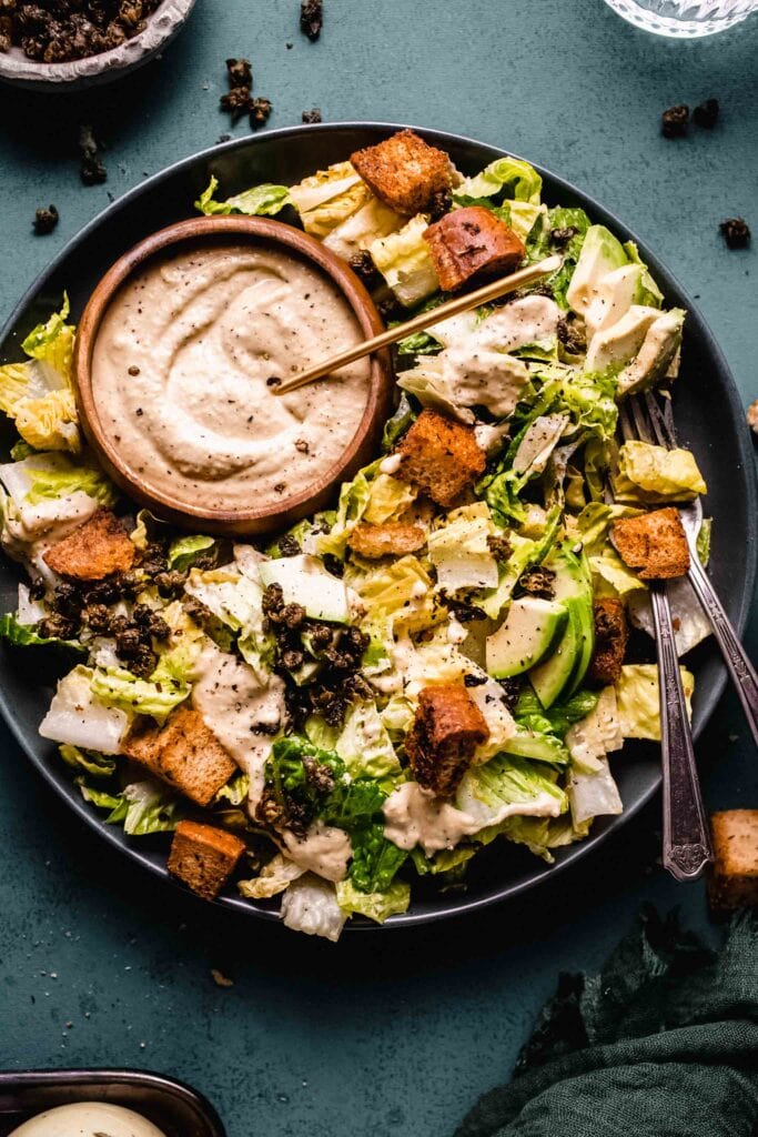 Overhead shot of vegan caesar salad on plate with small bowl of dressing.
