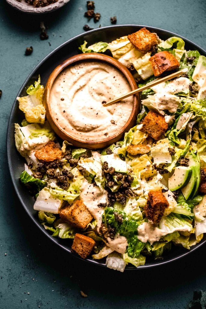 Prepared Vegan Caesar Salad next to bowl of fried capers. 