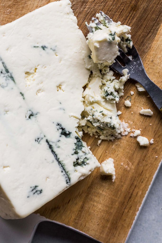Wedge of blue cheese on cutting board. 