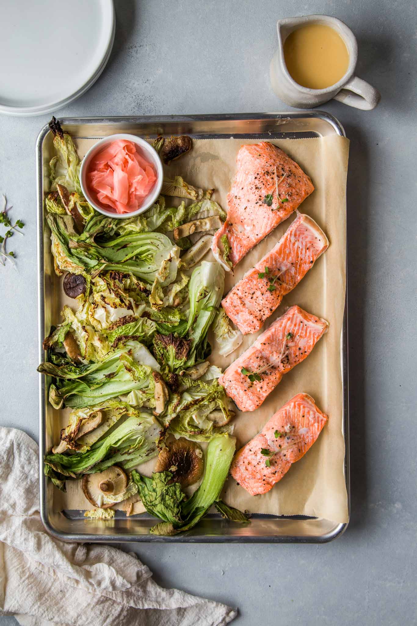 Sheet Pan Salmon out of oven next to roasted vegetables, ginger butter sauce and pickled ginger