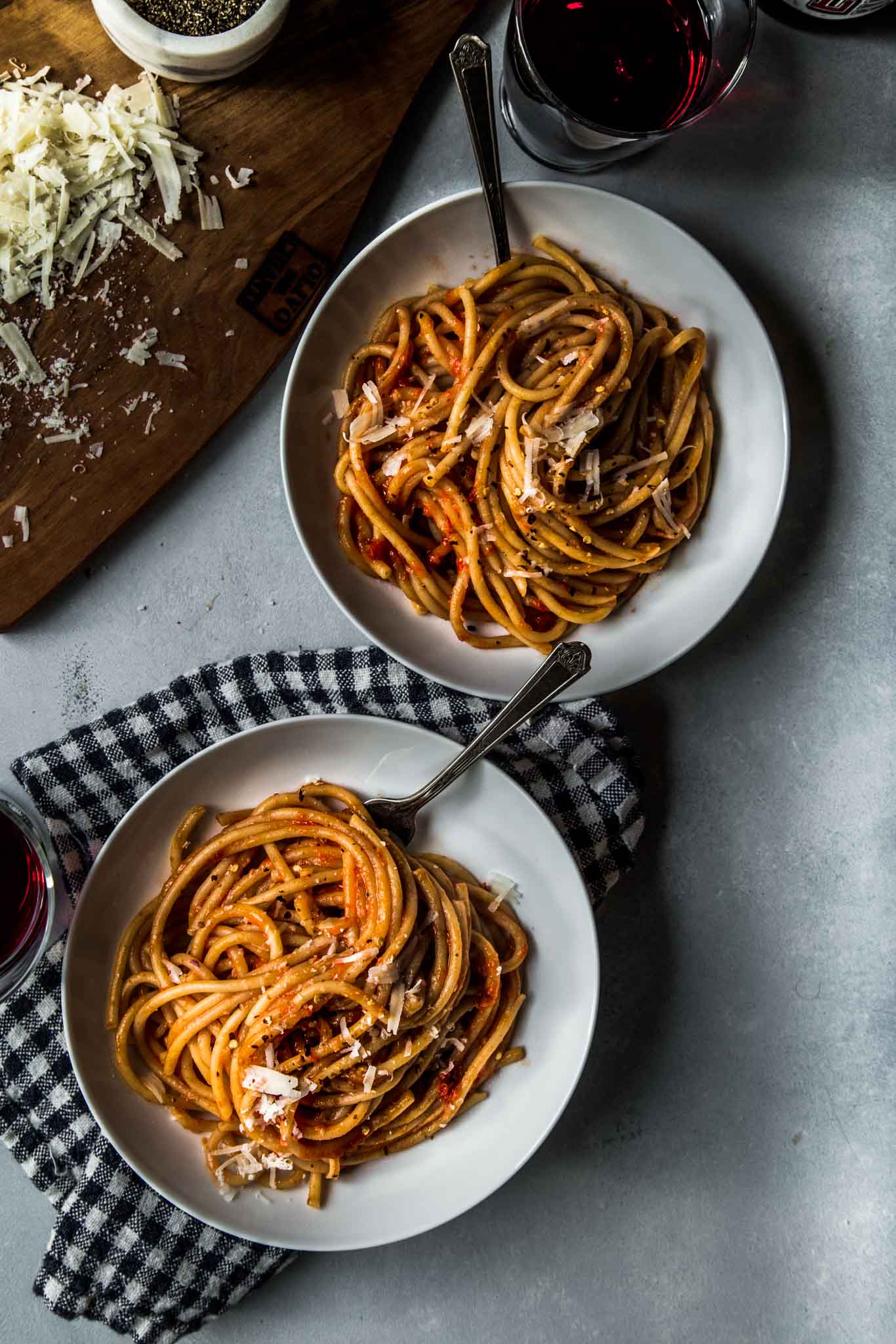 Two plates of pasta with roasted tomato sauce next to wine.
