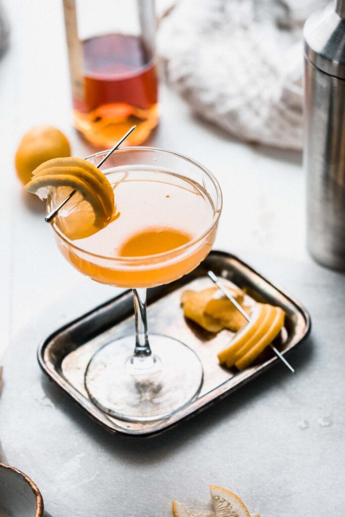 Applejack cocktail on small silver tray garnished with lemon slices.