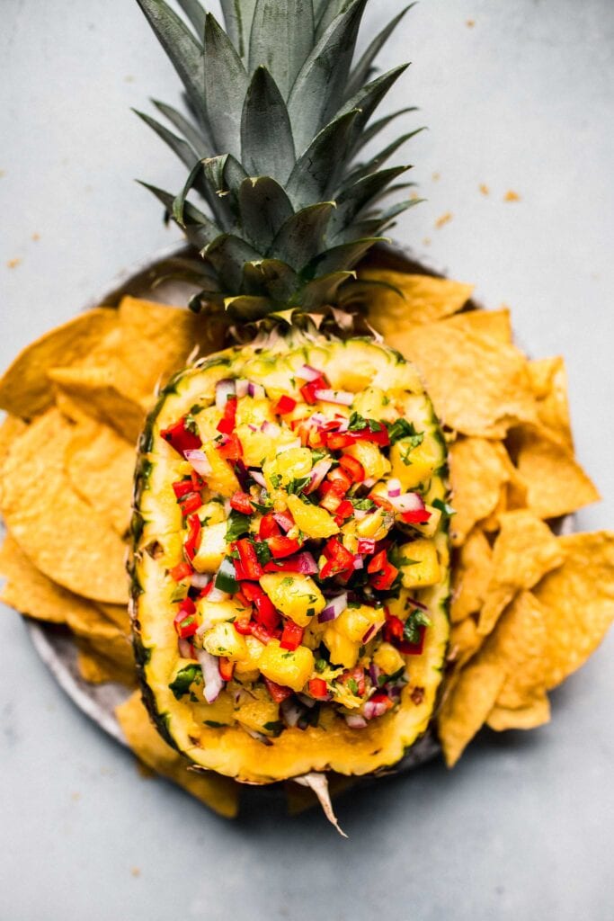 Pineapple salsa in pineapple bowl served with plate of tortilla chips. 