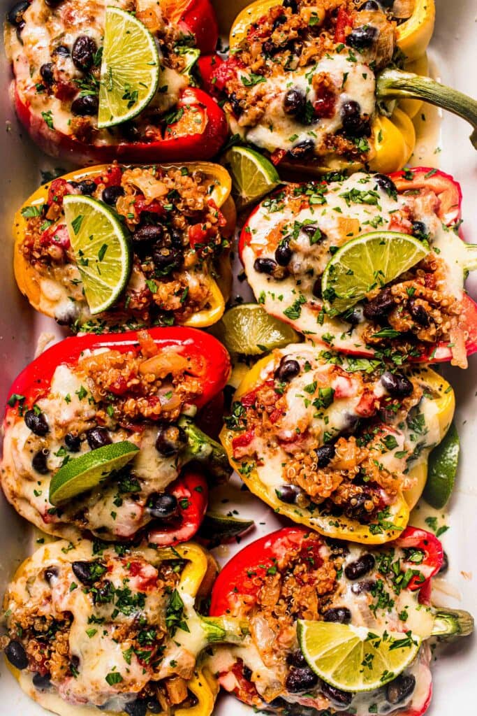 Baked stuffed peppers in dish with lime wedges. 