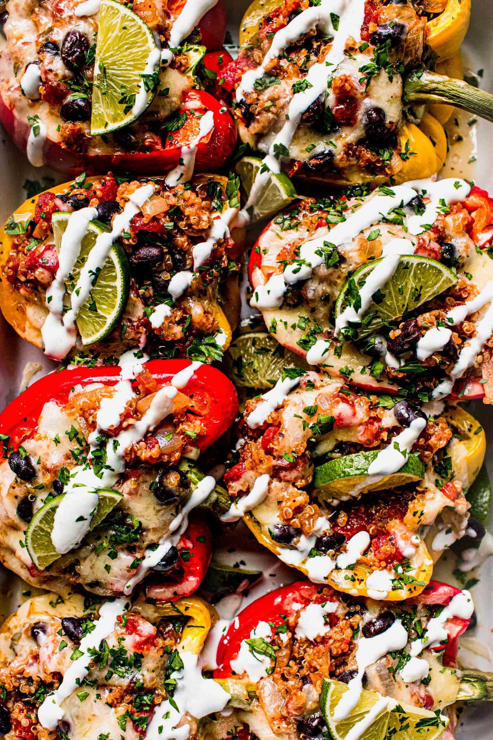 Baked quinoa stuffed peppers in baking dish with drizzle of sour cream.