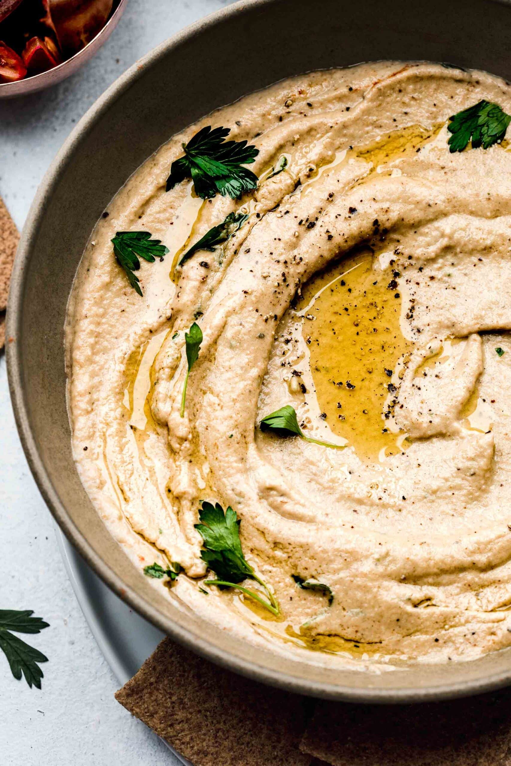 side view of bowl of baba ganoush topped with olive oil and parsley leaves.