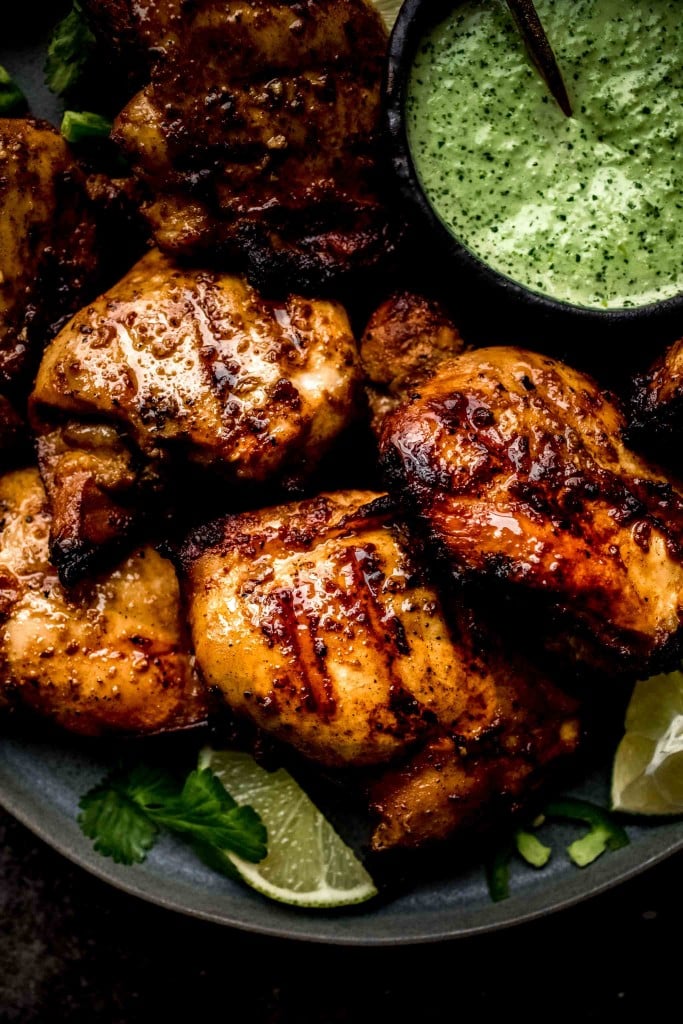 Close up of grilled chicken next to bowl of green sauce. 