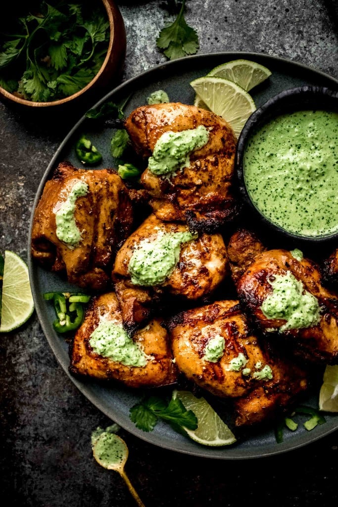 Plate of peruvian chicken with bowl of green sauce. 
