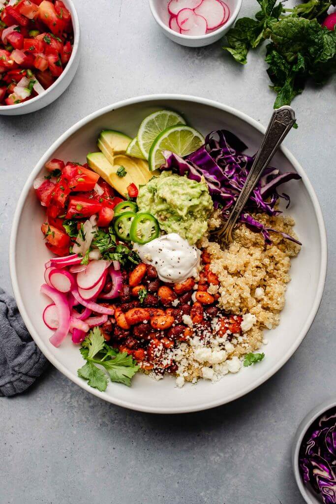 Quinoa topped with burrito bowl ingredients in white bowl with spoon.