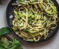 Overhead shot of dish of zucchini noodles with fresh herbs on a black plate.