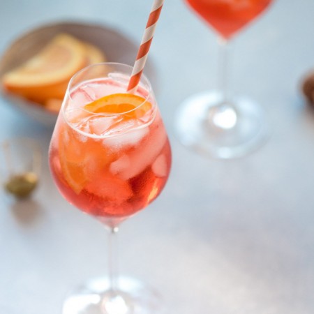 Aperol spritz cocktail in wine glass with orange and white straw