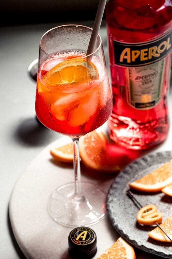 Bottle of aperol next to prepared spritz. 