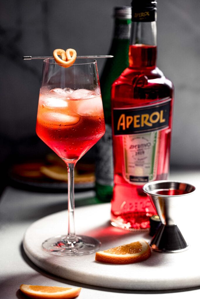 Aperol spritz garnished with orange rind skewered in the shape of a heart. 