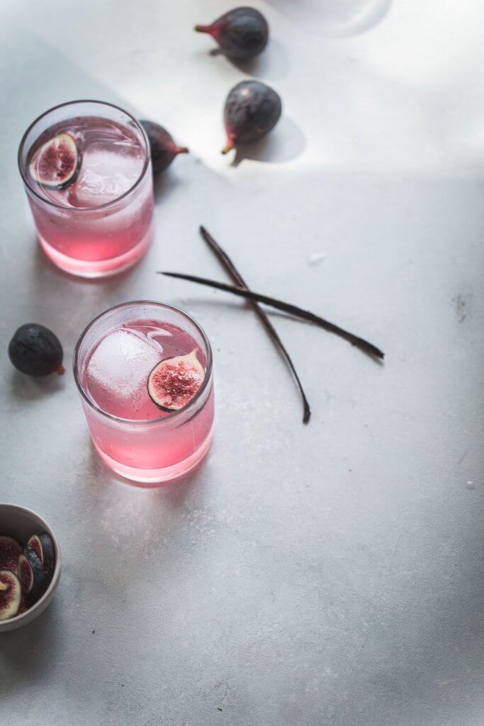Two fig cocktails next to vanilla beans and figs