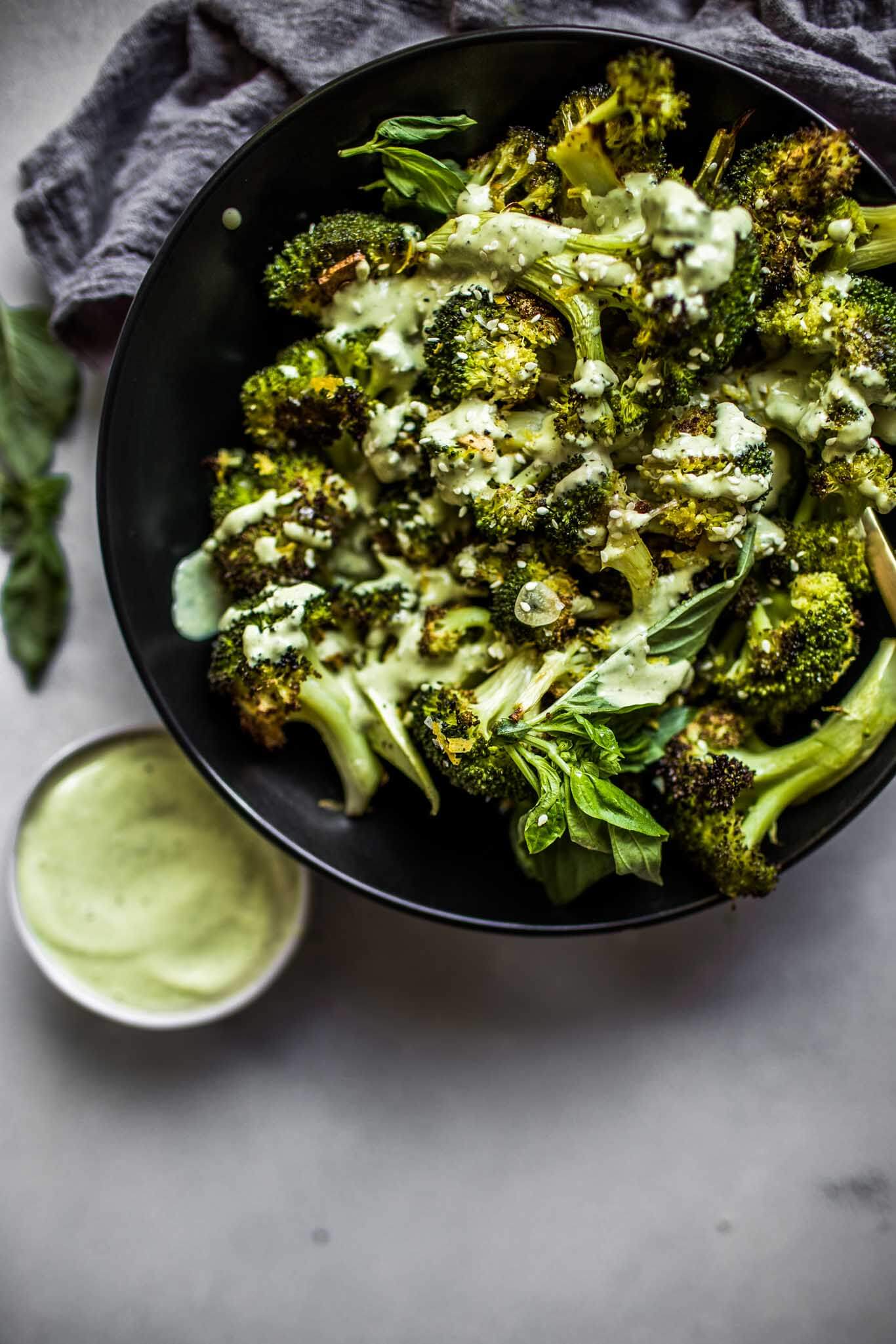 Overhead shot of roasted broccoli next to bowl of basil tahini sauce.